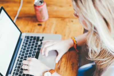 Kobieta pracująca przy laptopie w kawiarni, trzymając kawę