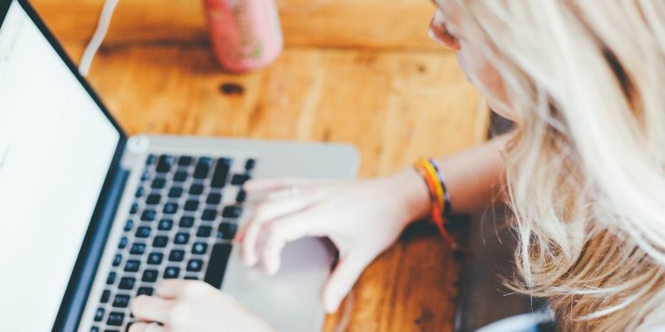 Kobieta pracująca przy laptopie w kawiarni, trzymając kawę