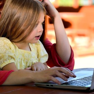 Matka pracuje na laptopie, trzymając na kolanach małą córkę