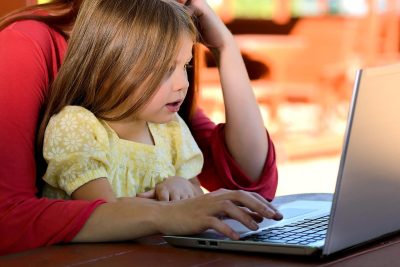 Matka pracuje na laptopie, trzymając na kolanach małą córkę