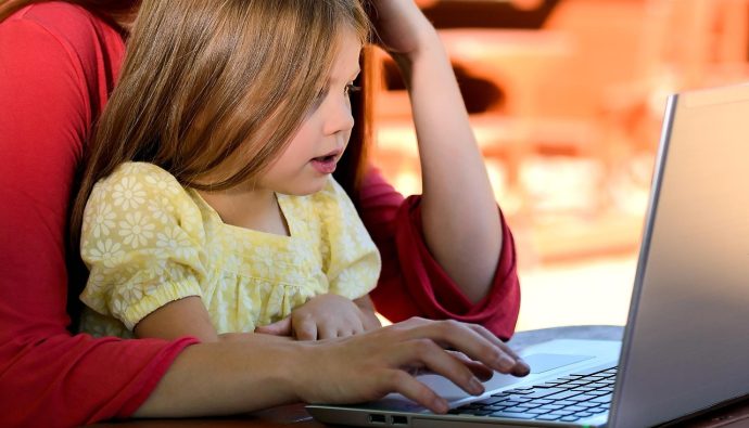 Matka pracuje na laptopie, trzymając na kolanach małą córkę