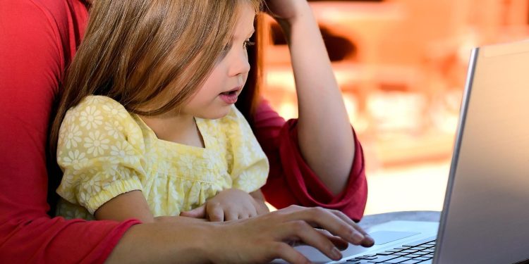 Matka pracuje na laptopie, trzymając na kolanach małą córkę